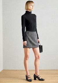 Svart polo-tröja, minikjol med hundtandsmönster, svarta klackar med dubbla remmar, och en liten svart handväska. Bakgrund med träplankor.