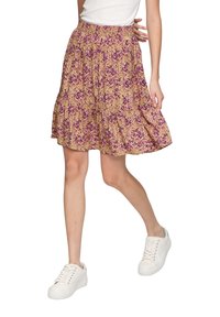 Beige Rock mit floralem Muster und lila Akzenten, mit einem gestuften Design und elastischem Taillenbund, kombiniert mit weißen Sneakers.