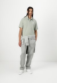 Light green polo shirt with short sleeves, gray sweatpants, and white sneakers. Gray sweatshirt draped around the waist.