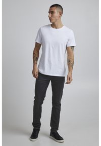 White cotton t-shirt with short sleeves, paired with dark denim jeans. The outfit is completed with black sneakers. Model stands facing left.