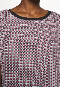 Röd och vit hjärtformat mönster på en svart bakgrund, med en slät tygtextur och en svart, rundad halsringning.