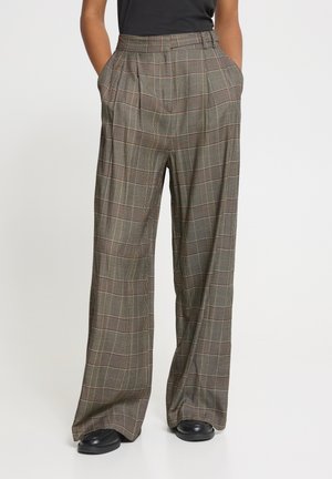 Pantalon à larges jambes à carreaux dans des tons gris avec des poches, porté avec des chaussures noires et un haut noir rentré.