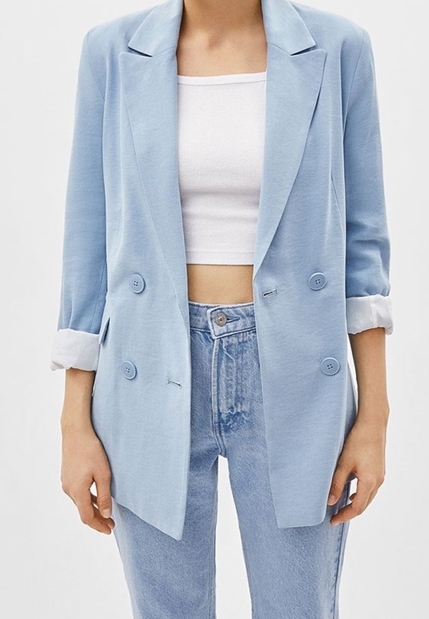 Světle modrá dvouřadá blejzr vyrobená z měkké tkaniny s ohrnutými rukávy, má dvě knoflíky a volný střih, kombinovaná s džínami s vysokým pasem.