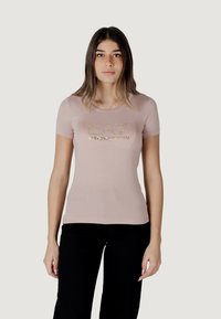 Camiseta ajustada de color rosa claro, hecha de una tela suave, con un estampado de logo metálico dorado en el pecho, mangas cortas y cuello redondo.