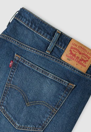 Tasca posteriore e cintura dei jeans Levi's 502 blu con etichetta in pelle del marchio e targhetta in tessuto rossa Levi's.