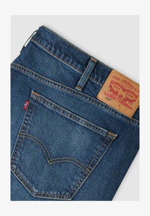 Tylnia kieszeń i pas niebieskich dżinsów Levi's 502 z skórzaną metką marki oraz czerwoną tkaną etykietą Levi's.