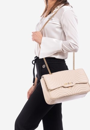 Béžová prošívaná kabelka s řetízkovým popruhem, s výrazným zakřiveným designem a zlatým logem. Materiál působí hladce a leskle.