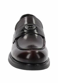 Mocassino in pelle marrone con una finitura lucida, caratterizzato da un emblema argento su una cinghia nera e cuciture rinforzate lungo il bordo.
