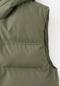 Olivno zeleni zimski jopič z kapuco. Gladka tekstura, z vodoravno šivom blizu dna in brez vidne kovinske opreme.