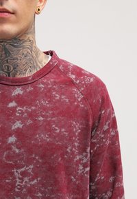 Sudadera color burdeos con un patrón texturizado y desvanecido, presenta un cuello redondo y mangas raglán. Está hecha de una tela suave y cómoda.
