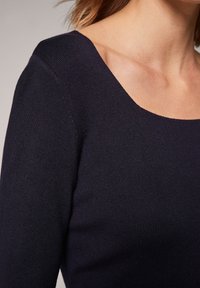 Haut en maille côtelée bleu foncé avec un décolleté carré et des manches longues, présentant une texture lisse et une coupe ajustée.