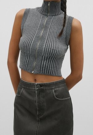Grijze mouwloze geribde gebreide crop top met hoge kraag en rits aan de voorkant, gecombineerd met een zwarte high waisted nepleren rok.
