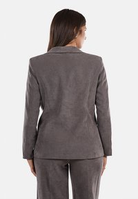 Blazer grigio in suede con una vestibilità su misura, design a un petto e revers a punta, caratterizzato da una texture liscia e una silhouette minimalista.