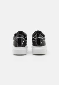 Sneaker in pelle verniciata nera con suole in gomma bianca, caratterizzate da un motivo testurizzato, tacchi arrotondati e logo "KARL LAGERFELD" sul tallone.