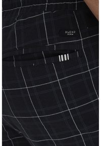 Černé kostkované kalhoty s bílými pruhy, vyrobené z měkké tkaniny, se zadní kapsou a štítkem s nápisem 'BLEND DENIM.'