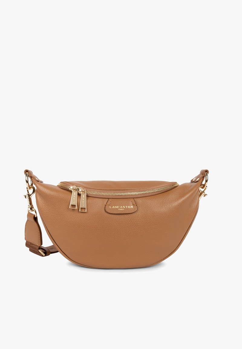 Tan leren crossbody tas met een ronde vorm, goudkleurige hardware, dubbele ritsluiting en een reliëflogo aan de voorkant.