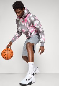 Grå hættetrøje med hætte og pink grafisk design, parret med grå shorts og hvide Nike-sko. Holder en basketball.