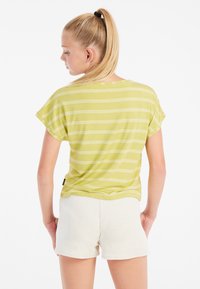 T-shirt verde a righe con maniche corte, caratterizzato da un collo rotondo. Indossato con pantaloni corti testurizzati color crema.