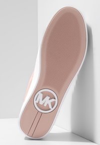Suola di sneaker rosa e bianca con grip testurizzato, logo rotondo con le iniziali "MK" vicino al tallone, fotografata su uno sfondo angolare bianco.