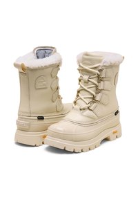 Bottes d'hiver beiges imperméables avec une doublure en fausse fourrure, un design à lacets, et une semelle épaisse et texturée. Comprend un logo et des accents matériels hexagonaux.