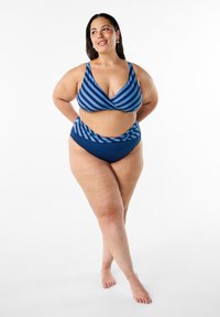 Divdaļīgs bikini, izgatavots no zilas auduma ar horizontālām svītrām. Augšdaļai ir dziļa V-veida kakla izgriezums, savukārt augstās jostasvietas apakšdaļai ir salocīšanas dizains.