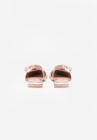 Σαμπό από ροζ χρυσό λουστρίνι με λουράκι στον αστράγαλο, ανοιχτή πλάτη και επίπεδο τακούνι, διαθέτοντας λεία υφή και μινιμαλιστικό σχέδιο.