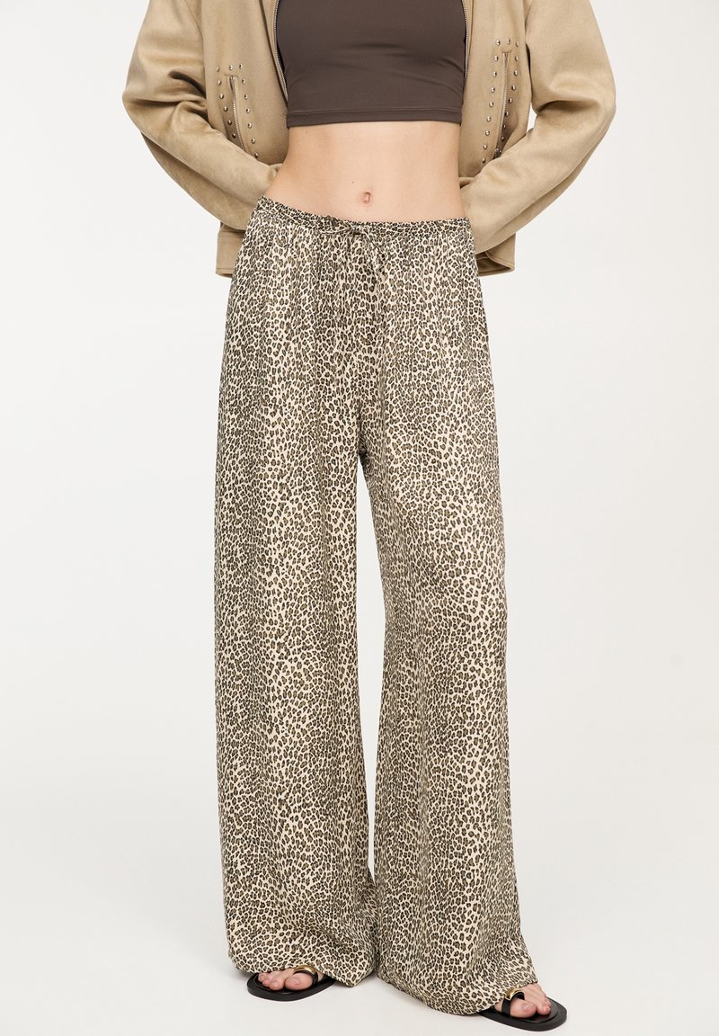 Pantalon à jambes larges imprimé léopard en tissu léger avec une taille élastique et un cordon de serrage. Mis en valeur par des sandales ornées d'un détail doré.