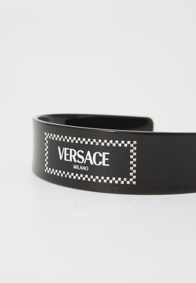 Juodas plastikinis plaukų lankelis su blizgiu paviršiumi. Savybė - stačiakampio formos logotipas su "VERSACE MILANO" baltos spalvos, apipavidalintas mažais sidabro spalvos taškais.