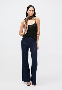 Black chevron-patterned camisole paired with navy wide-leg pants featuring a textured knit. Accessorized with a multicolored patterned scarf.