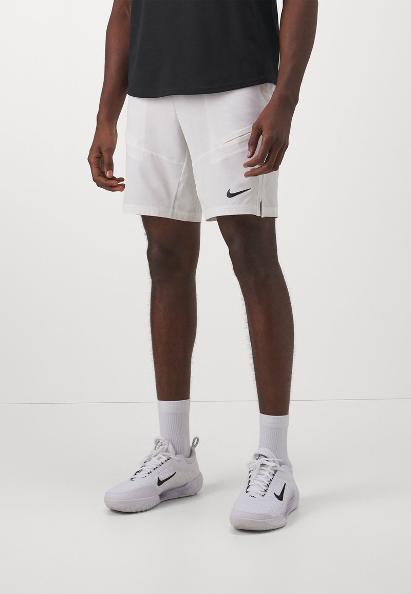 Bermudas blancas de Nike hechas de material liviano con bolsillos laterales y un logo negro. Combinadas con zapatillas blancas y calcetines hasta el tobillo.