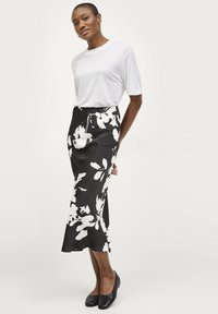 Jupe noire à motifs floraux blancs, conçue avec une silhouette évasée. Associée à un t-shirt blanc uni et des ballerines noires.