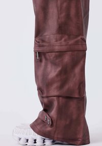Donker bordeaux, stoffen broek met textuur, voorzien van een ritszak en knoopaccenten bij de enkel, gecombineerd met een wit sneaker.