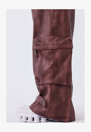 Pantalons en tissu texturé bordeaux foncé, avec une poche zippée et des accents de bouton au niveau de l'ourlet, associés à des baskets blanches.