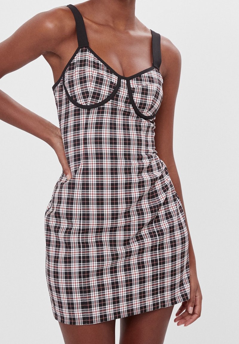 Svart och röd rutig klänning med formade kupor, tjocka svarta remmar, en figursydd bodice och rynkade sidodetaljer. Slät tygtextur.