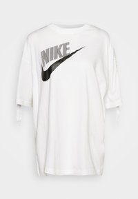 Camiseta blanca de gran tamaño hecha de algodón. Presenta un logo de Nike negro con un diseño en zigzag, mangas cortas y tirantes laterales.