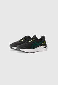 Chaussures de sport noires avec une tige texturée, des accents verts et des semelles blanches. Elles disposent de lacets et d'un design léger.