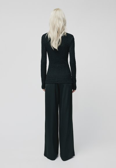 Top lungo nero strutturato con maniche lunghe abbinato a pantaloni neri a gamba larga. Il top presenta una silhouette aderente, mentre i pantaloni hanno un design ampio e fluido.