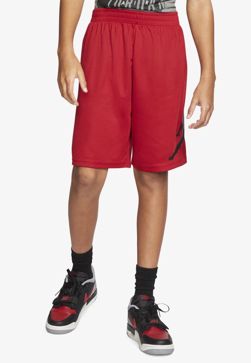 Pantalones cortos deportivos rojos con una cinturilla elástica, combinados con zapatillas negras y rojas que tienen una parte superior texturizada y cierres de cordones.