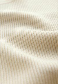 Tela beige acanalada con textura vertical y pliegues suaves, mostrando un detalle en primer plano de la superficie del material.
