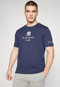 Granatowa koszulka z krótkim rękawem z logo New York Yankees w białym kolorze, z brandingiem Champion na prawym rękawie.