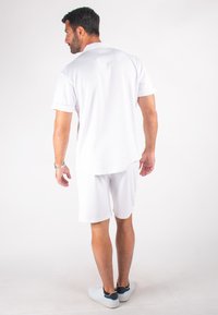 Chemise polo blanche et shorts en matériau respirant, dotés de manches courtes et d'un ourlet arrondi, associés à des chaussures blanches.