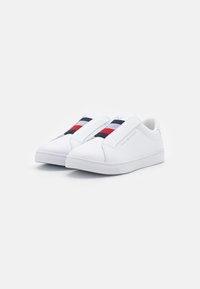 Weiße Leder-Slipper mit kontrastierenden roten und navy-blauen elastischen Bändern, Gummisohle und minimalistischem Design mit Logo der Marke.