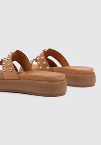 Sandalias de plataforma marrones con acentos de correas con tachuelas, parte superior de cuero suave y plantilla acolchada. Forma redondeada y suela de goma gruesa.
