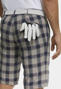 Mannen shorts met ruitpatroon in blauw, wit en bruin, voorzien van een geweven witte riem. Vier witte golfhandschoenen zijn in de achterzak gestoken.