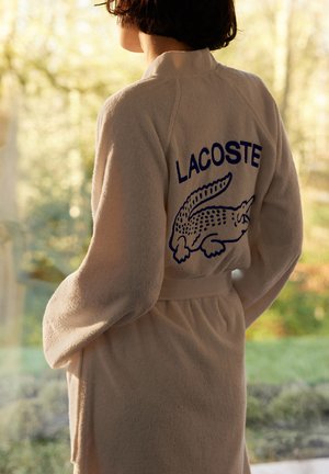Accappatoio in spugna beige con logo Lacoste blu e design di coccodrillo, vita cinchata e maniche lunghe.