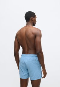 Világoskék fürdőnadrág elasztikus derékpánttal, hátsó zsebbel és sima textúrával, hátulról látható egy modellen.