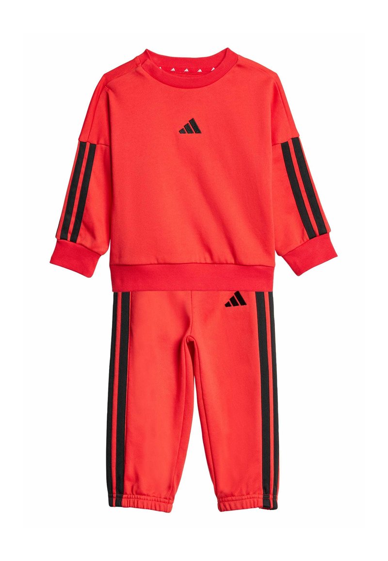Czerwony zestaw bluz i spodni wykonany z miękkiego materiału, z czarnymi paskami na rękawach i bokach, z logo Adidas na górze i dole.