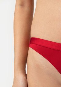 Czerwony dół bikini o gładkiej, elastycznej fakturze i błyszczącej talii. Ma minimalistyczny design, z niskim krojem.