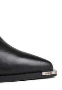 Scarpa in pelle nera con punta affusolata, dotata di una piastra metallica sul bordo della suola incisa con il nome del marchio "BRONX".