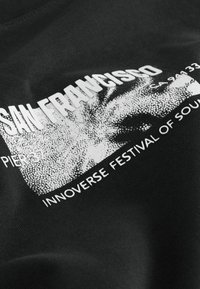 Schwarzer Stoff mit weißem Text "SAN FRANCISCO", "PIER 37" und "INNOVERSE FESTIVAL OF SOUND" neben einem pixeligen Grafikdesign.